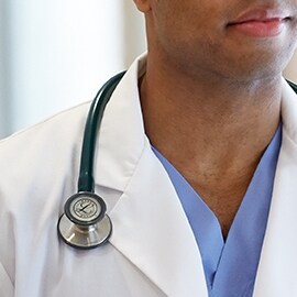 Littmann stetoskop koji se nosi pravilno sa spoljne strane kragne belog mantila sprečavajući kontakt između creva stetoskopa i vrata kliničara.